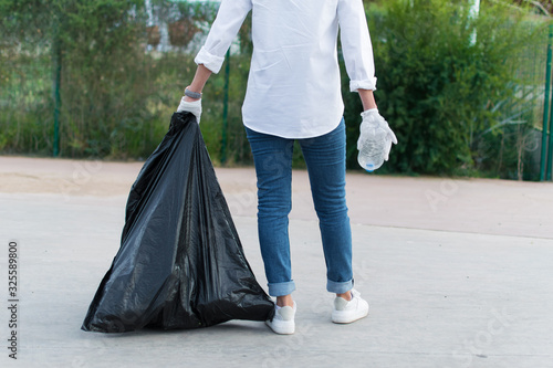 Person holding a trash bad and a plastic bottle