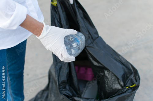 Woman in white globes puting plastic bottle in trash bag