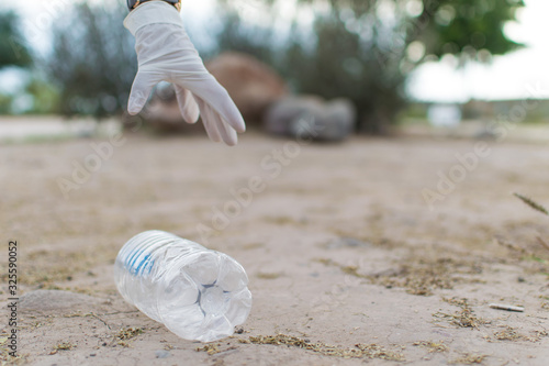 Hand in white gloves taking a plastic bottle from the floor