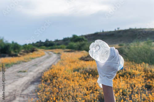 Raised hand holding a plastic bottle in natural environment
