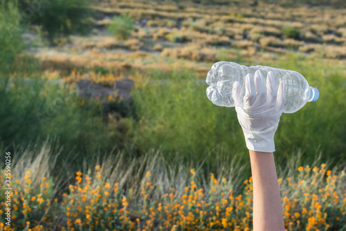 Raised hand holding a plastic bottle in natural environment