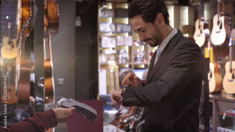 An upwardly mobile Middle Eastern man using a mobile phone - smartwatch to purchase product at the point of sale terminal in a retail store with nfc identification payment for verification