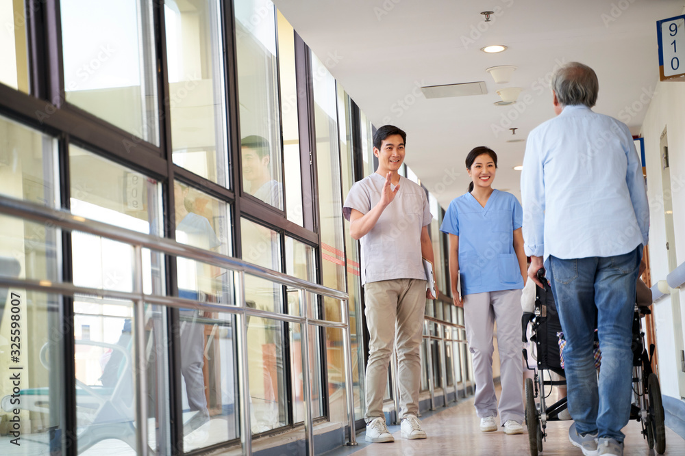 asian employee greeting residents in hallway of nursing home