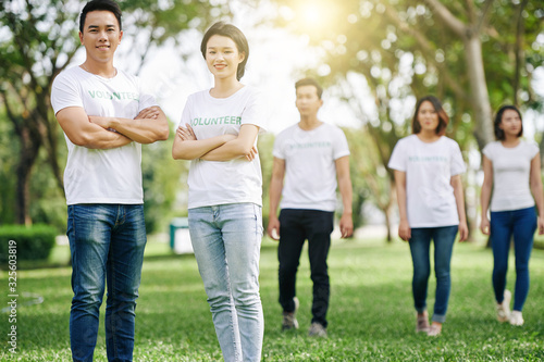 Happy young Asian volunteers standing with arms folded after cleaning garbage in city park