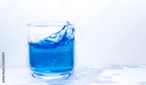 Blue drink water splash in clear glass on white background 