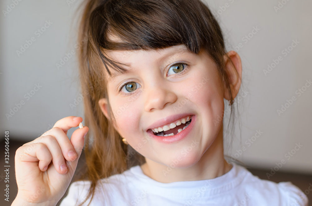 Cute preschooler showing her milk tooth fell out and her growing permanent tooth in open mouth. Beautiful smiling preschool girl holds in hand her first dropped baby tooth. Dental hygiene concept Cute preschooler showing her milk tooth fell out and her growing permanent tooth in open mouth. Beautiful smiling preschool girl holds in hand her first dropped baby tooth. Dental hygiene concept