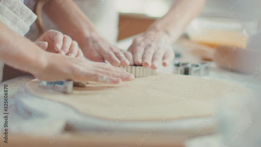 Close up woman and girl hands cutting dough with cookie cutters on kitchen table Close up woman and girl hands cutting dough with cookie cutters on kitchen table
