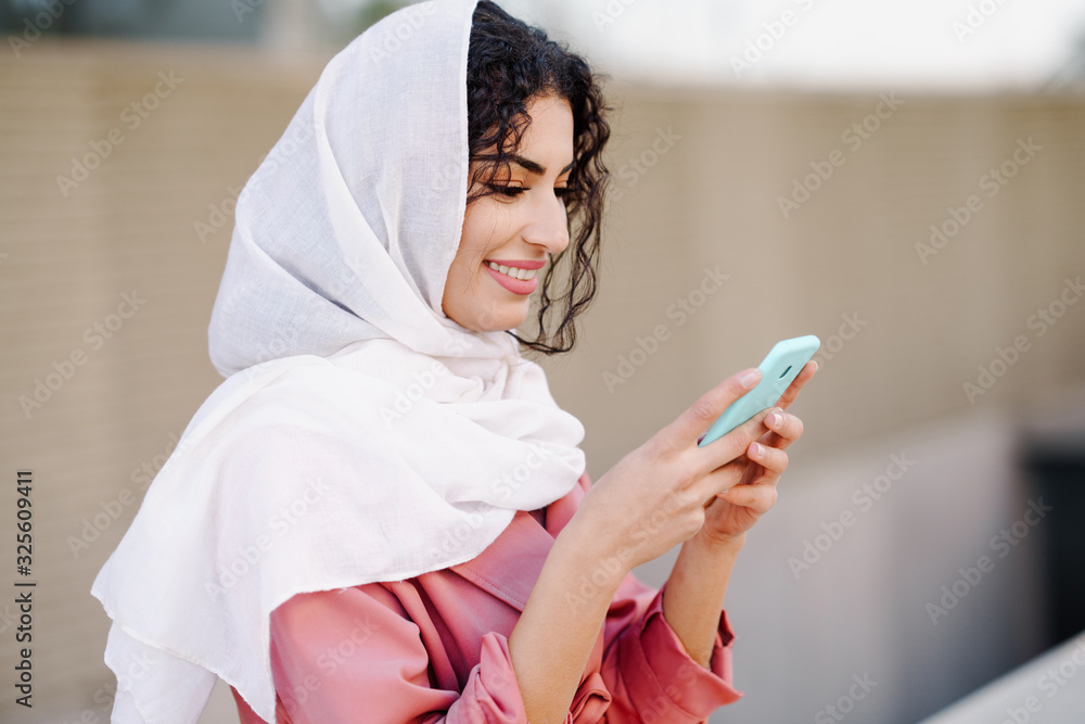 Young Muslim woman wearing hijab texting message with her smartphone. Young Muslim woman wearing hijab texting message with her smartphone.