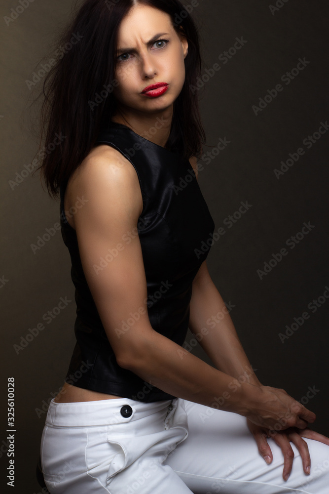 a brunette in a black leather sleeveless blouse poses on a gray background a brunette in a black leather sleeveless blouse poses on a gray background
