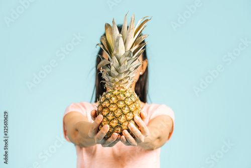 Young woman is holding a fresh and delicious pineapple and posing isn studio front of a blue font isolated.  photo