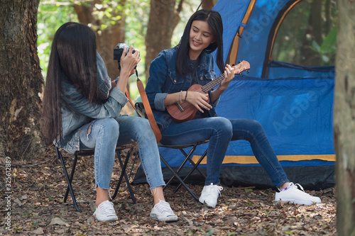 Group of teenage asian girls camping and resting at forest playing ukulele and take a photo happy together. Camping concept