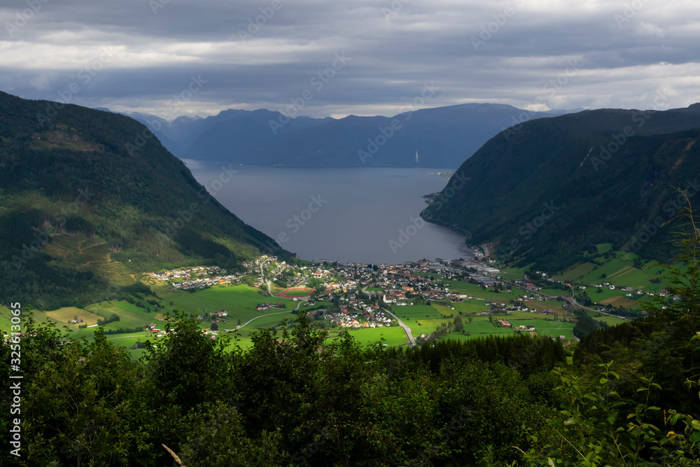 View of the village of Vikøyri on the southern shore of the Sognefjorden, Vik commune in Norway on a cloudy day.  The sun light struggle through clouds illuminating the village. Travel destination.