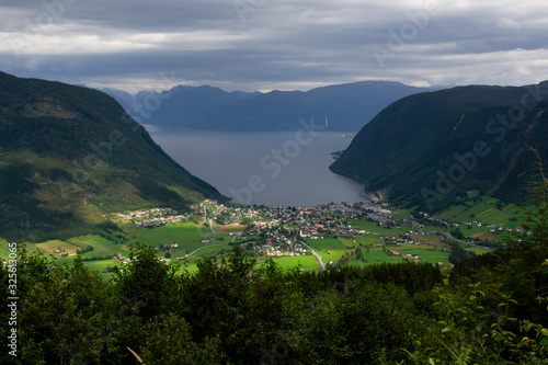 View of the village of Vikøyri on the southern shore of the Sognefjorden, Vik commune in Norway on a cloudy day.  The sun light struggle through clouds illuminating the village. Travel destination. © maxfluor