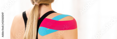 Rear view of a female patiet with kinesio tape on her shoulder. Kinesiology, physical therapy, rehabilitation banner.