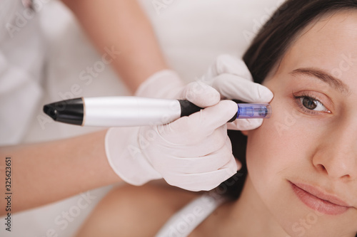Cropped shot of a professional cosmetologist using dermapen on her female client. Young woman receiving mesotherapy treatment photo