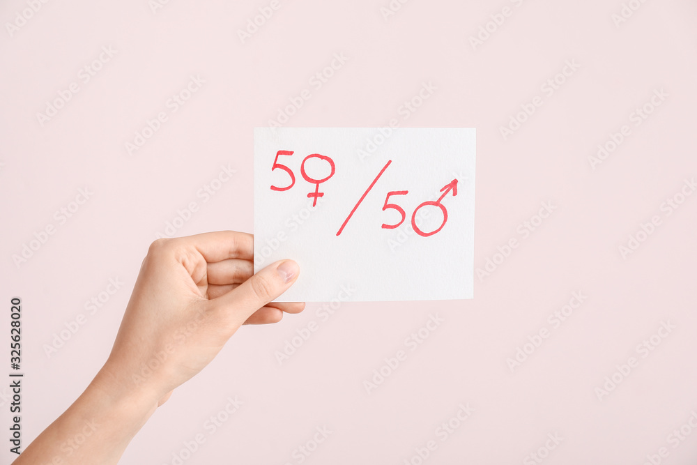 Female hand holding paper sheet with simple fraction and symbols of woman and man on color background. Concept of feminism Female hand holding paper sheet with simple fraction and symbols of woman and man on color background. Concept of feminism