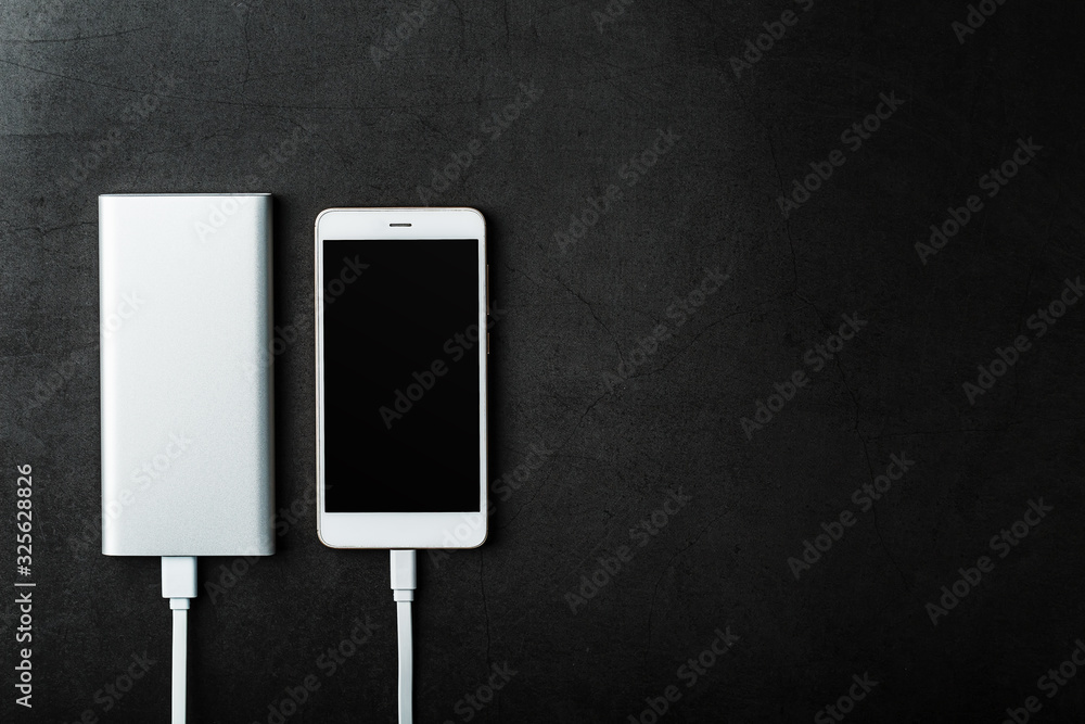Power Bank charges your smartphone on a dark background. Universal external battery for gadgets free space and minimalistic composition. Power Bank charges your smartphone on a dark background. Universal external battery for gadgets free space and minimalistic composition.