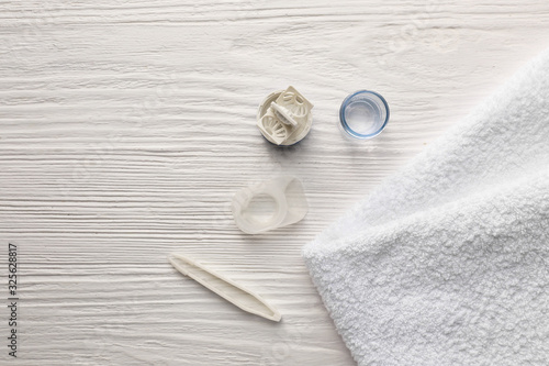 Container for contact lenses, tweezers and towel on white wooden background