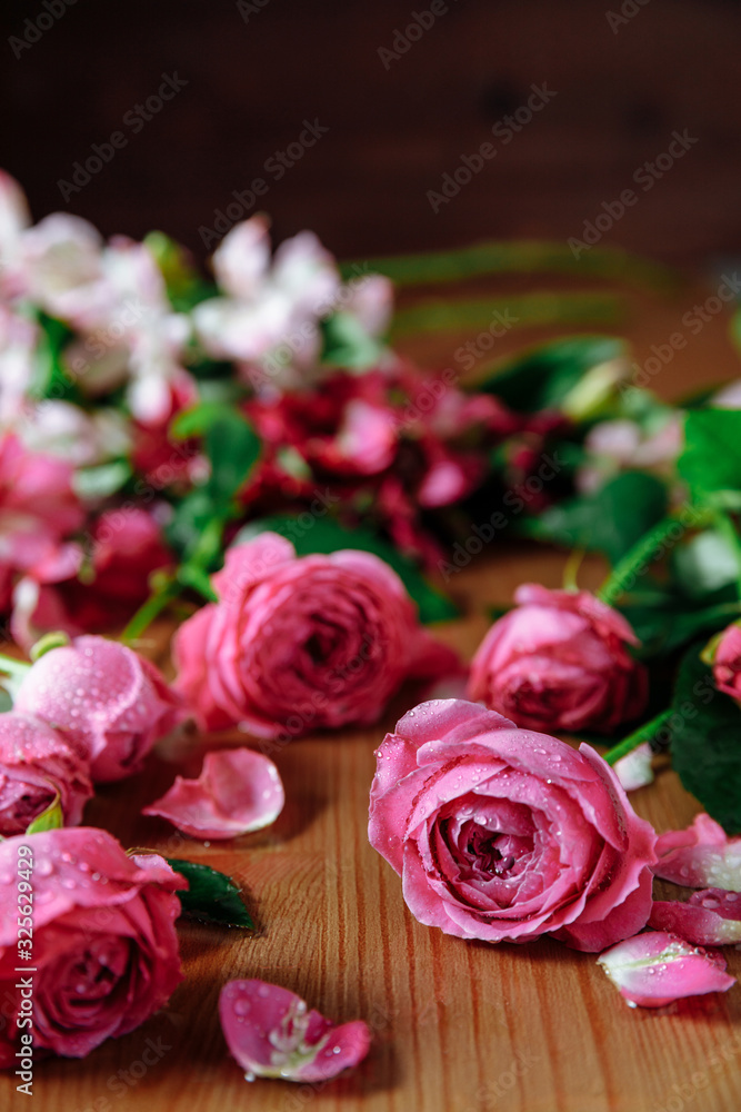 Fresh pink roses flowers with petals an leaves on the wooden table and dark black background. Still life Fresh pink roses flowers with petals an leaves on the wooden table and dark black background. Still life