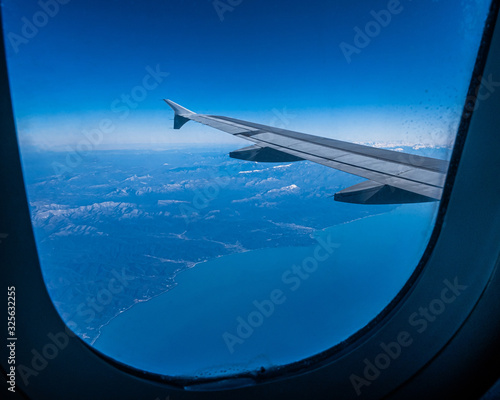 View of the wing of an airplane flying over the mountains and the sea