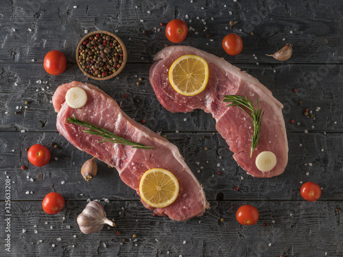 Two large pork steaks with lemon, tomatoes, spices and garlic on a wooden table. The view from the top.