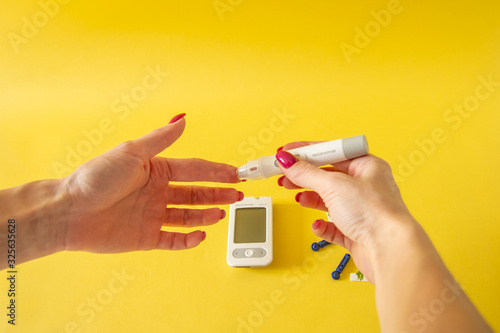 Diabet. Medical equipment. Medical concept. Close up of woman hands on yellow background using lancet on finger to check blood sugar level by Glucose meter 