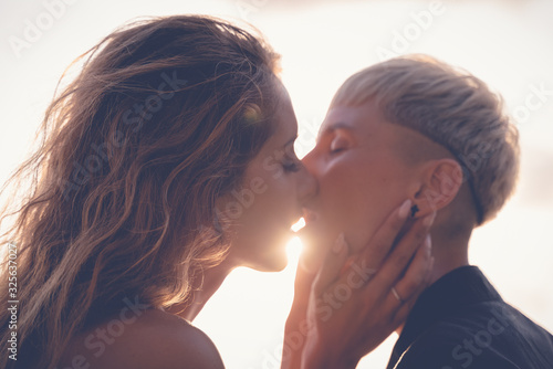 Two beautiful young women gently passionately kiss on the lips, face close-up. In the rays of the setting sun Love tenderness attraction concept..