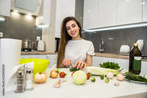 Girl posing at a kitchen table while prepares a salad of different vegetables and greens for a healthy lifestyle.