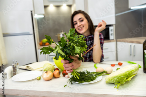 Girl posing at a kitchen table while prepares a salad of different vegetables and greens for a healthy lifestyle.