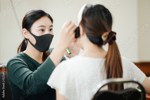 Make up artist wareing mask work in studio salon. Woman applying by professional make up master. 