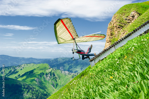 Bilde på lerret Hang glider pilots launches from steep slope high in the mountains