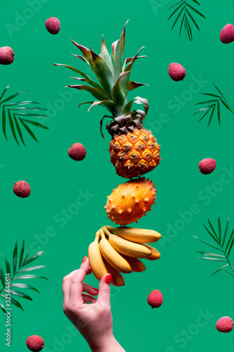 Assortment of tropical fruits, pyramid balancing o human hand on green background. Pineapple, kiwano, kiwi , lichee and banana - tower made of exotic fruits. photo