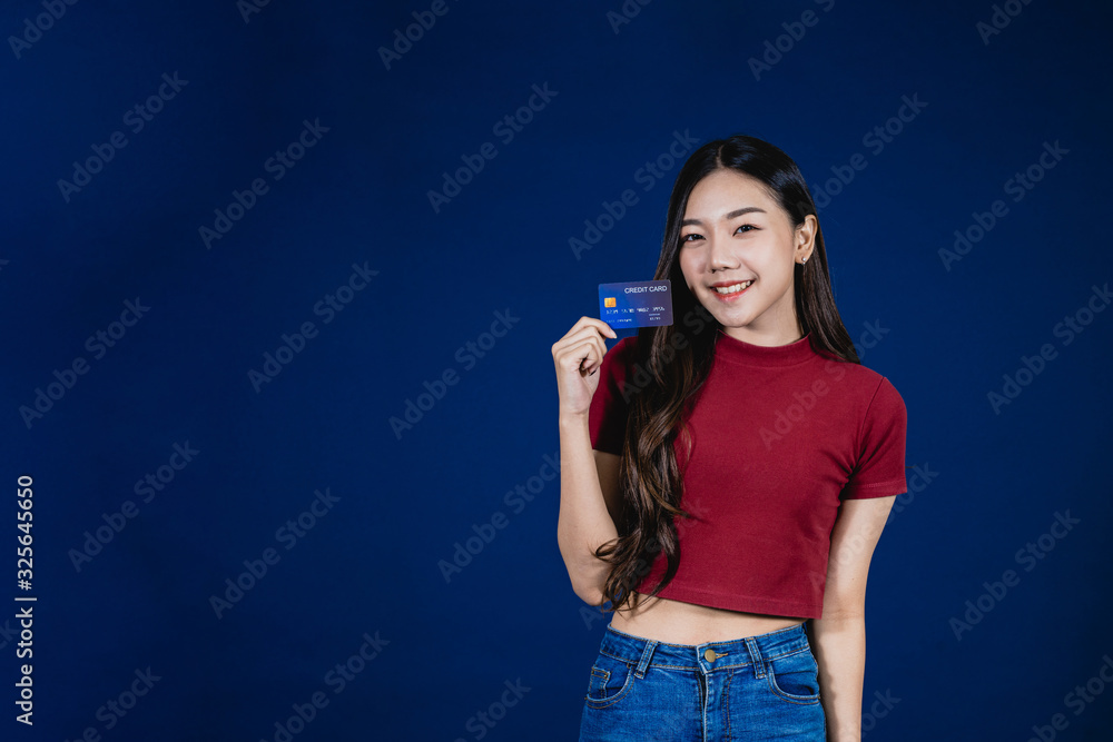 Portrait of Asian beautiful young woman presenting credit card with smile face isolated blue background. The girl standing and looking at camera in studio. Advertisement & presentation concept. Portrait of Asian beautiful young woman presenting credit card with smile face isolated blue background. The girl standing and looking at camera in studio. Advertisement & presentation concept.