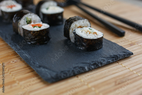Sushi rolls with salmon, tuna, avocado, rice in algae and chopsticks on a dark board lying on a bamboo mat.