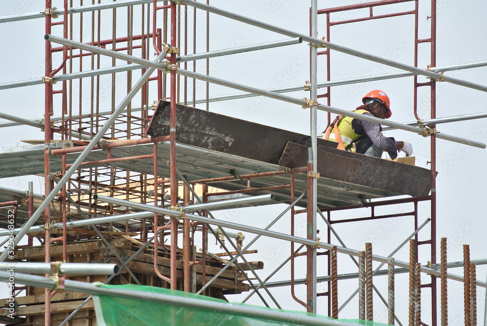 Construction workers wearing safety harness and installing scaffolding at high level in the construction site.