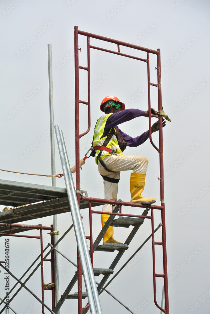 Construction workers wearing safety harness and installing scaffolding at high level in the construction site.