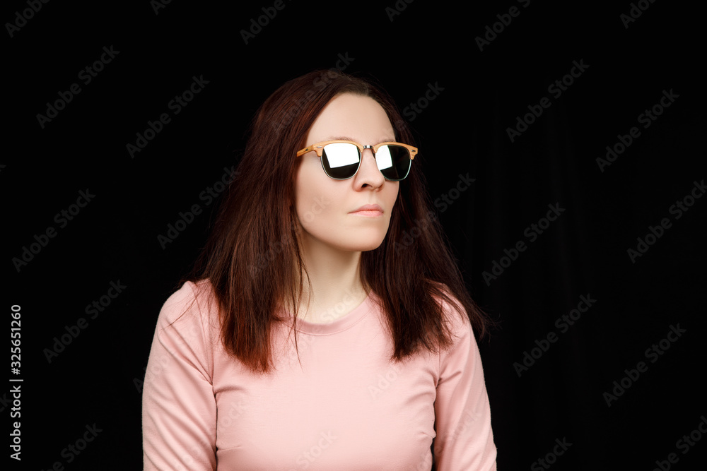 Image of sweet confident young lady standing over black background in studio, wearing pink blouse and fashionable eyeglasses, having long brown hair Image of sweet confident young lady standing over black background in studio, wearing pink blouse and fashionable eyeglasses, having long brown hair