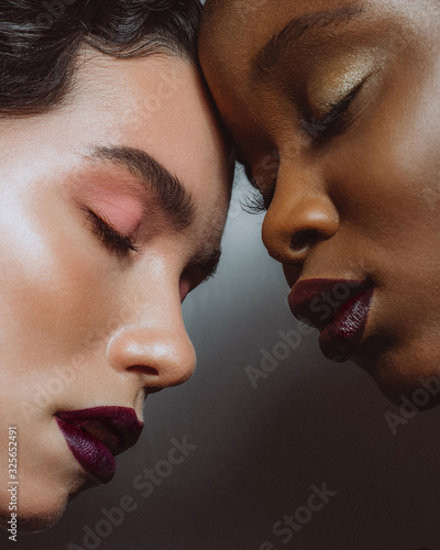 Portrait of africans and europeans girls with bare shoulders and fashionable make up stand close to each other on a white background
