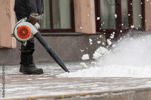 Фотография Man cleans street from snow with blower