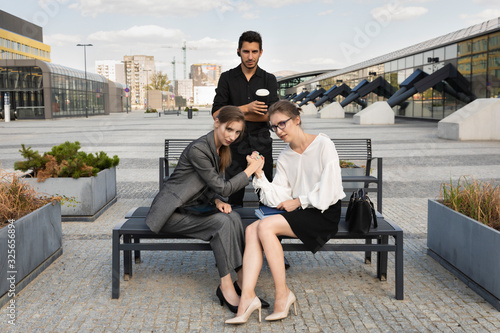 Business partners on the background of an office building. Two women compete with each other, while a man simply watches what is happening. © Liliia