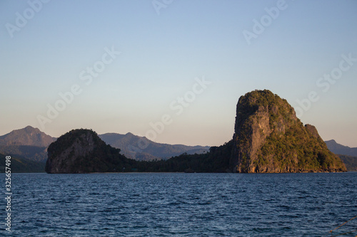 Scenic seascape with islands and mountains on horizon in the evening. Beautiful calm sunset in Philippines. Evening seascape panorama. Tropical lagoon. Peaceful sunset on beach. © Nataliia