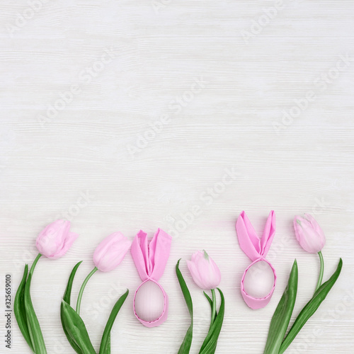 Fototapeta Naklejka Na Ścianę i Meble -  Easter composition with handmade pink easter eggs with ears from rabbit and fresh flowers tulip on white wooden background with copy space. View from above, flat lay.