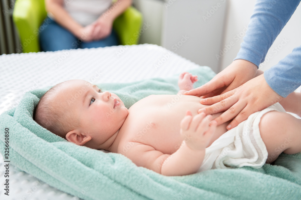 © andreaobzerova - Female massage therapist or a doctor examining newborn baby boy with the mother watching in the background. Baby massage concept. © andreaobzerova - Female massage therapist or a doctor examining newborn baby boy with the mother watching in the background. Baby massage concept.