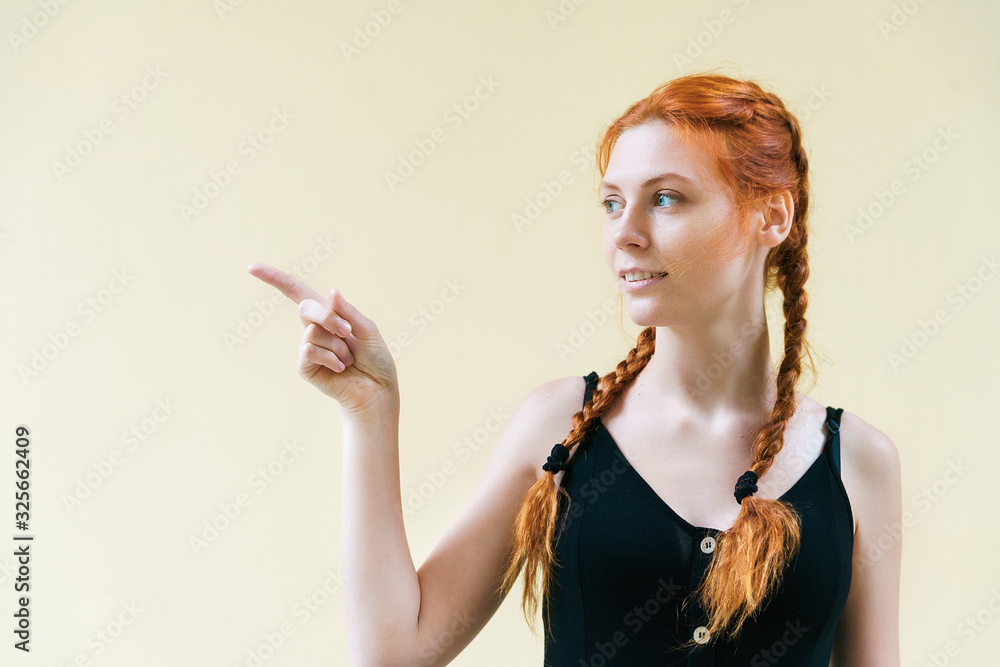 Obraz premium Expressive facial expressions emotions. Red haired girl in black dress on yellow background show finger to side.