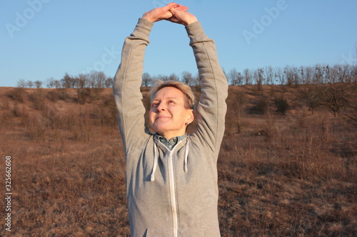Happy smiling young woman  breathing fresh air and doing exercise in nature. Spring outdoor activities