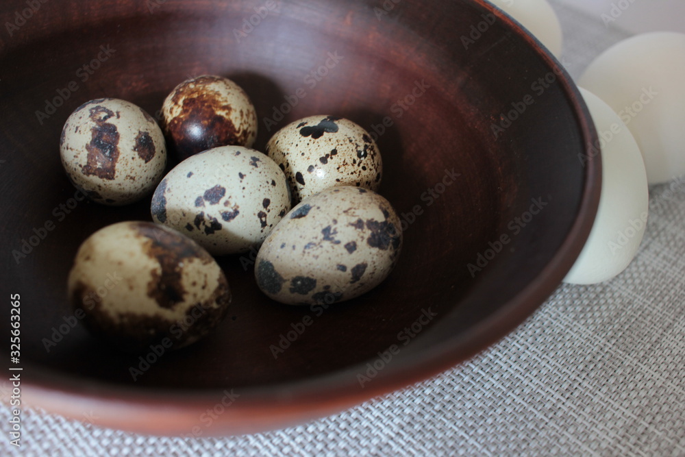 Obraz premium Quail eggs in a brown ceramic bowl and white chicken eggs on a white texture background