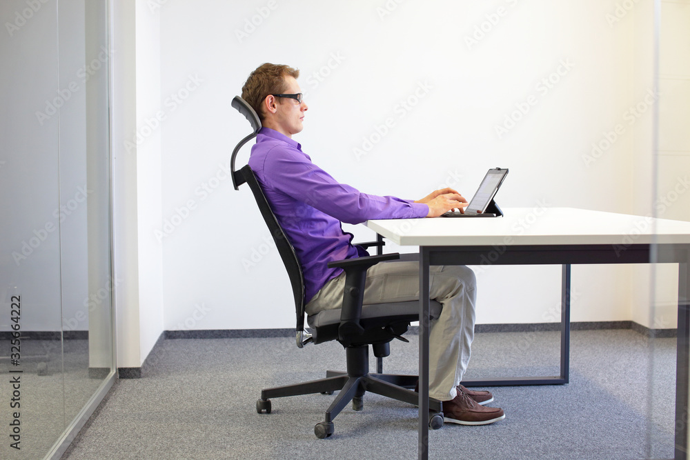 correct sitting position at the office desk . man on chair working with tablet correct sitting position at the office desk . man on chair working with tablet