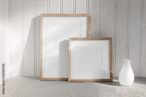 Two portrait and square wooden frame mockups. Linen cloth and modern ceramic vase with in sunlight. White beadboard wainscot wall paneling background. Scandinavian interior, home design. Art concept.