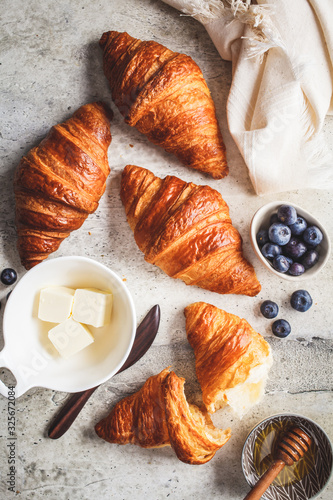 Fresh croissants with blueberries, butter and honey, gray background, top view.