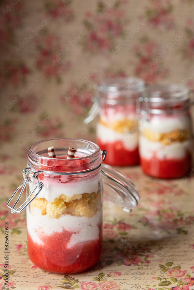 rot weißer Erdbeer Käse Sahne Kuchen im Glas mit Boden Biscuit auf geblümten Grund rot weißer Erdbeer Käse Sahne Kuchen im Glas mit Boden Biscuit auf geblümten Grund